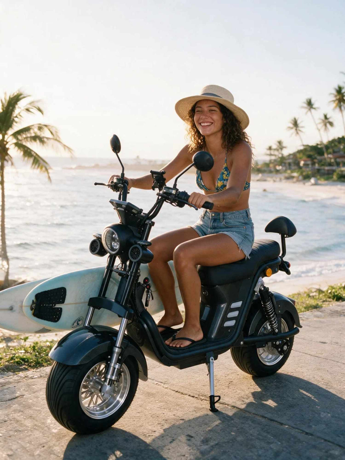 Uma mulher sorridente usando chapéu de palha e biquíni sentada na scooter elétrica ZORYKEN M8-3000 com uma prancha de surfe ao fundo, em uma avenida à beira-mar.