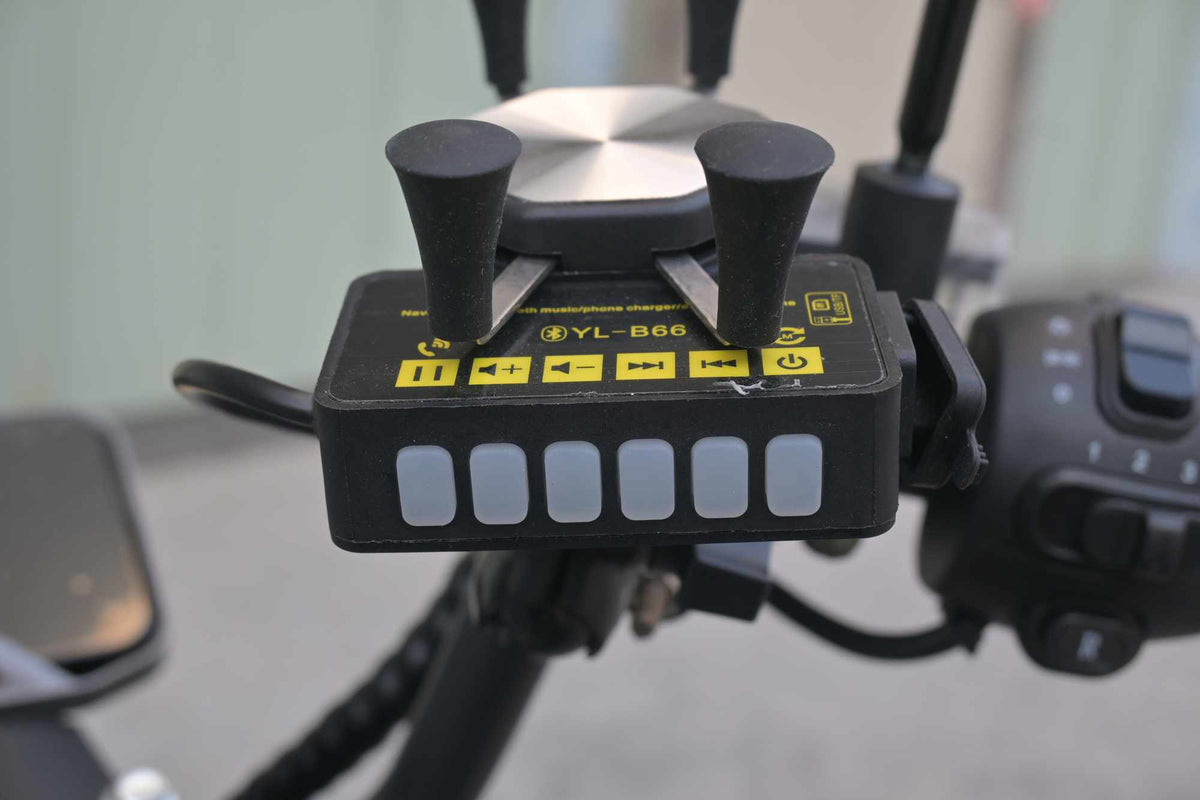 Detalhe frontal do painel do suporte de celular YL-B66, exibindo os botões emborrachados para ligar, pausar, avançar músicas e ajustar o volume do alto-falante Bluetooth.