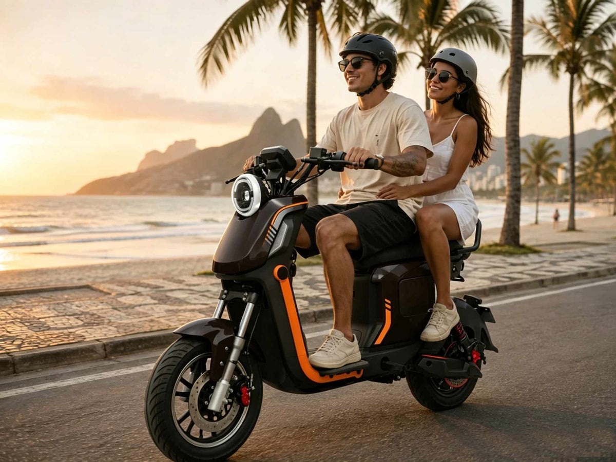 Um casal usando capacete e óculos de sol sorri ao andar em uma scooter elétrica ZORYKEN Z6 marrom escura em uma ciclovia à beira-mar com coqueiros e montanhas ao fundo durante o pôr do sol. O veículo possui detalhes laranjas na carenagem e freio a disco dianteiro.