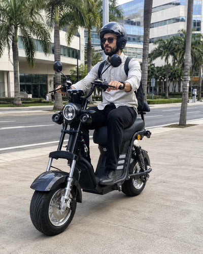Homem de capacete, óculos de sol e mochila pilotando a scooter elétrica ZORYKEN M8-3000 preta em uma rua da cidade, demonstrando seu uso para mobilidade urbana.