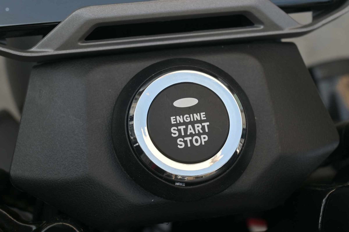 Detalhe em close do botão cromado com a inscrição "ENGINE START STOP" para o sistema de partida com um toque da scooter elétrica ZORYKEN M8-3000.
