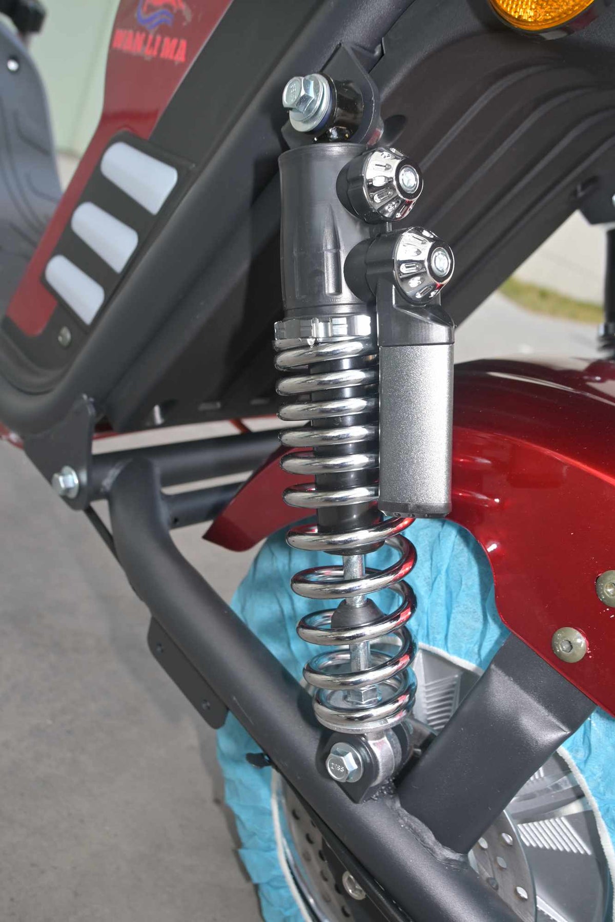 Detalhe em close do sistema de suspensão dupla traseira da scooter ZORYKEN M8-3000, destacando o amortecedor de mola cromado com reservatório extra, fixado ao quadro de ferro e próximo ao para-lama vermelho.